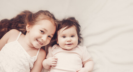 Two smiling sisters lying on the white blanket indoors