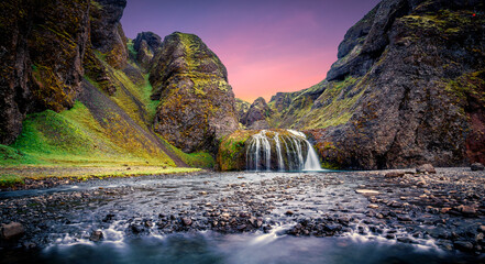 Fototapeta na wymiar Wonderful nature of Iceland. fresh green grass and icelandic moss near river with waterfall. Tipical Icelandic scenery during sunset. Dramatic Scene of Stjornarfoss Waterfall with colorful sky