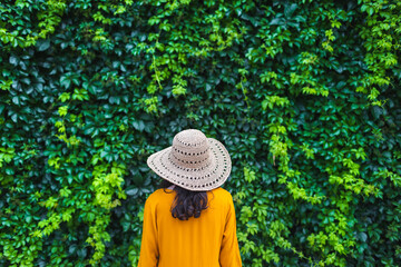 A girl in a straw hat stands near a wall overgrown with ivy