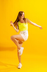 Fototapeta na wymiar Cheerful young girl, student dancing isolated on bright yellow background. Concept of beauty, art, fashion, emotions and facial expressions