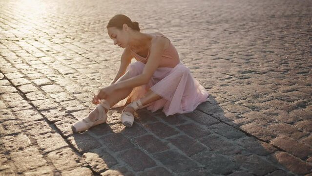 Beautiful ballerina ties up pointe shoes ribbons around leg