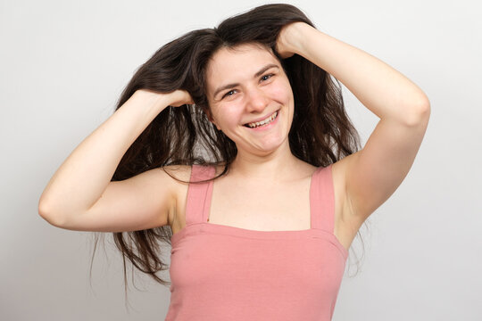 A beautiful brunette woman with long hair on a white background holds her hands on her head and thinks about what hairstyle to do