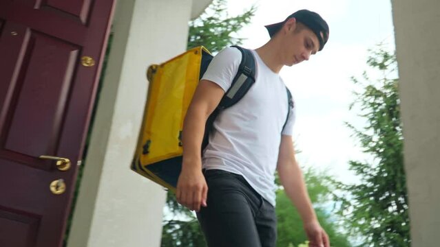 Side view Caucasian delivery boy passing order to client at door walking away. Live camera follows courier delivering food and drink leaving. Convenience and service concept