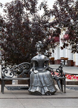 Silver sculpture of a beautiful young lady on a bench in the historical center of Omsk in summer