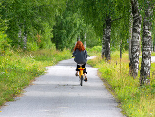 Unidentified red haired girl riding a bike on a summer day via walkway.