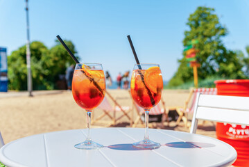 Two glasses of orange spritz aperol drink cocktail on table outdoors with sea and trees view...