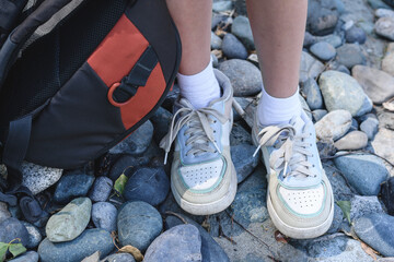The concept of traveling with a backpack, an active lifestyle. Legs of a young girl traveler in sneakers with a sports backpack