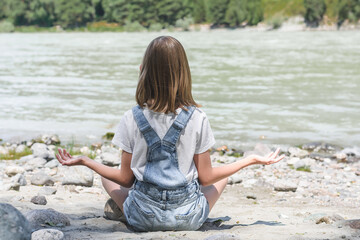 A girl in the mountains is sitting in the lotus position, doing sports, meditating outdoors. A healthy lifestyle.
