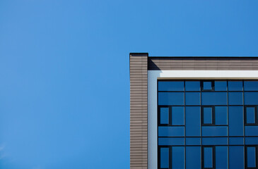 Fototapeta premium The edge of the facade of a modern building with glass mirrored windows against the blue sky. Place for text