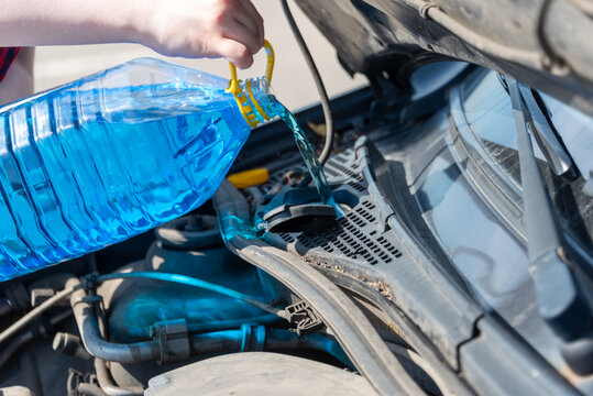 Woman hands pouring blue windshield washer fluid into a car's tank.