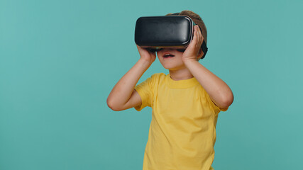 Little toddler children boy using headset helmet app to play simulation game. Watching virtual reality 3D 360 video film. Young preschool kid in VR goggles isolated alone on blue studio background