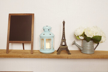 Eiffel tower statue, blue lantern, flower in metal vase and empty blackboard for copy on wooden shleves
