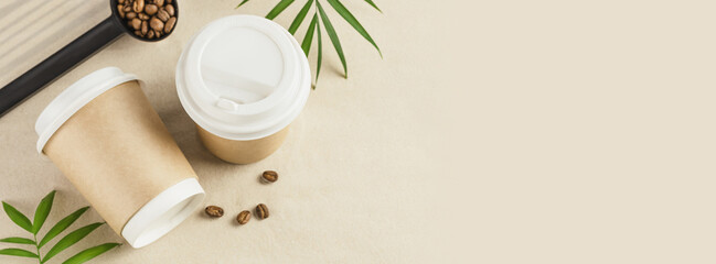 Coffee to go banner. Two disposable eco-friendly cardboard cups with coffee beans on the sand with palm leaves and copy space. Takeaway coffee concept. Vacation with coffee. Banner size