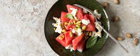 a bowl of watermelon with feta cheese and pistachios on a light table