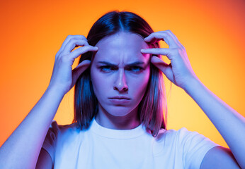 Closeup face of young annoyed girl looking at camera isolated on orange color background in neon light. Concept of emotions, facial expressions
