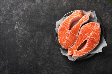 Salmon. Raw salmon steak. Fresh raw salmon fish with cooking ingredients, herbs and lemon prepared for grilled baking on black background. Healthy food. Top view. Copy space.