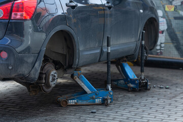 Replacing wheels on old black car, two jacks hold the body in the raised position