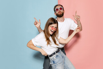 Young stylish happy man and excited girl dancing hip-hop at studio on blue and pink trendy color...