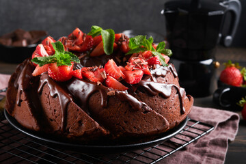 Dark Chocolate Bundt Cake with Ganache Icing and strawberry on dark stone or concrete table background. Festive cake. Selective focus