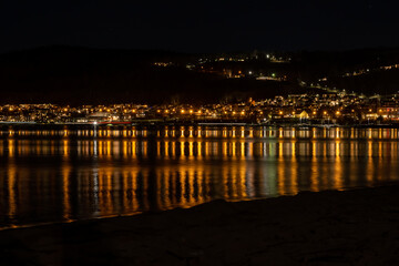 Fototapeta na wymiar Lights from a hillside town reflect in a lake at night