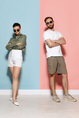 Obraz premium Fashionable couple, handsome man and charming girl posing isolated over blue-pink background. Fashion, emotions, youth, love, travel, vacation concept