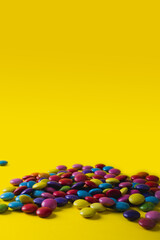Obraz premium Pile of colorful chocolate candies with copy space against yellow background