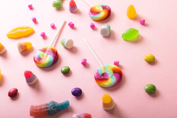 High angle view of multi colored sugar candies and lollipops scattered over pink background