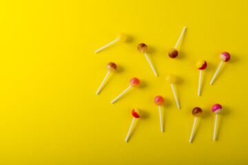 Overhead view of lollipops scattered by copy space against yellow background - Powered by Adobe