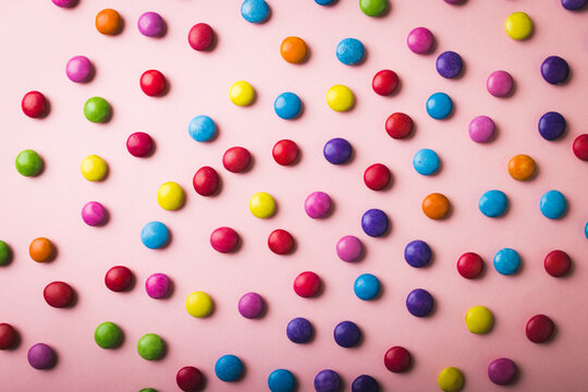 Directly above view of multi colored chocolate candies scattered on pink background
