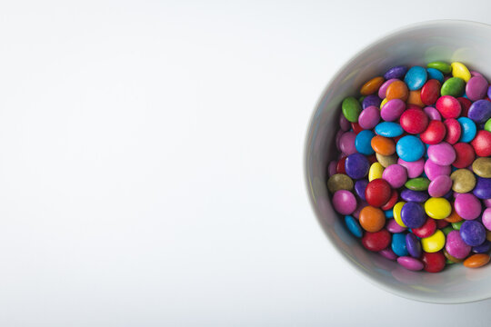 Directly above view of copy space by multi colored chocolate candies in bowl on white background