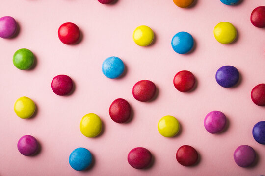 Directly above view of multi colored chocolate candies scattered over pink background