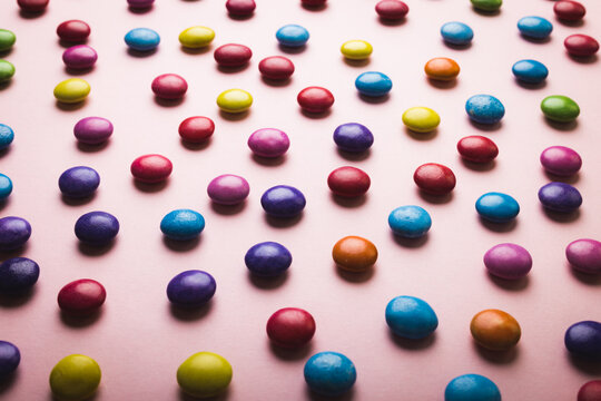 High angle full frame view of multi colored chocolate candies scattered on pink background