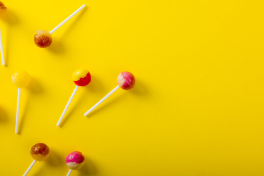 Directly above view of lollipops scattered by copy space over yellow background