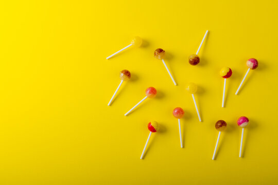 Overhead view of lollipops scattered by copy space against yellow background