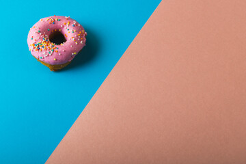 High angle view of fresh pink donut with sprinklers by copy space on two tone colored background