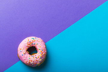 Directly above view of fresh pink donut with sprinklers by copy space against two tone background