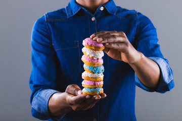Midsection of african american man holding fresh donut stack against gray background