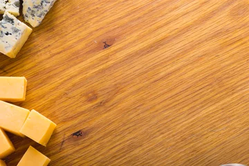 Fotobehang Overhead view of various cheese slices on wooden board, copy space © wavebreak3