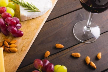 Tuinposter High angle view of red wine by cheese and grapes with almonds on wooden table, copy space © wavebreak3