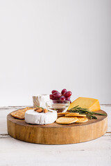 Cheese by grapes with herbs and crackers on wooden board against white background, copy space