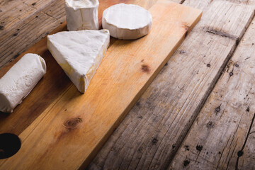 High angle view of brie cheese of various shape on wooden board, copy space