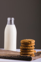 Milk in glass bottle with stack of cookies against gray background, copy space