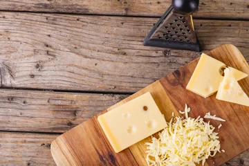 Tuinposter Overhead view of grated cheese on wooden board by grater at table, copy space © wavebreak3
