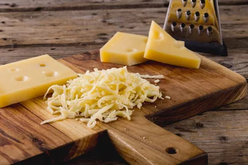 Tuinposter Grated cheese on wooden board by grater at table, copy space © wavebreak3