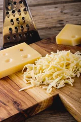 Tuinposter Close-up of grated cheese on wooden board by grater at table, copy space © WavebreakMediaMicro