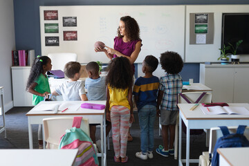 Multiracial elementary school students looking at caucasian young female teacher showing brain model
