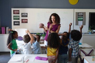 Multiracial elementary students raising hands while caucasian young teacher showing brain model