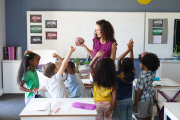 Multiracial elementary students raising hands during caucasian young teacher showing brain model