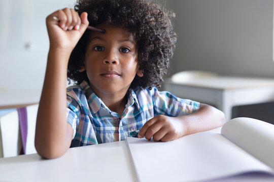 Portrait of african american elementary schoolboy holding pencil while sitting at desk in classroom