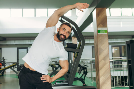 Portrait of an athlete in the gym. A man wearing a white T-shirt is smiling and doing exercises